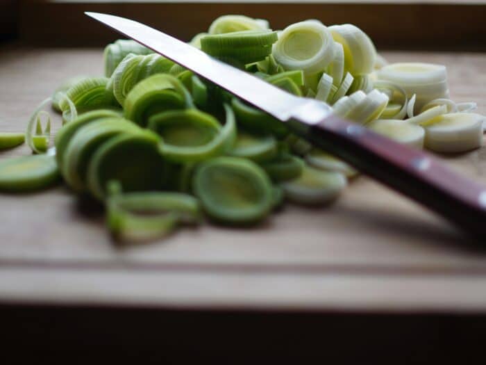Freshly sliced leeks on a wooden cutting board with a sharp knife, ideal for cooking and food preparation themes.