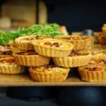 A tempting display of homemade quiches topped with fresh ingredients on a wooden tray.