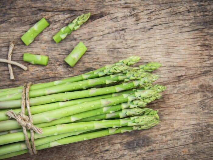 Bundle of fresh organic asparagus on a rustic wooden table, showcasing vibrant green colors and natural texture.