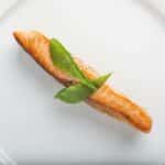 Elegant dish of grilled salmon fillet with green garnish on a white plate.
